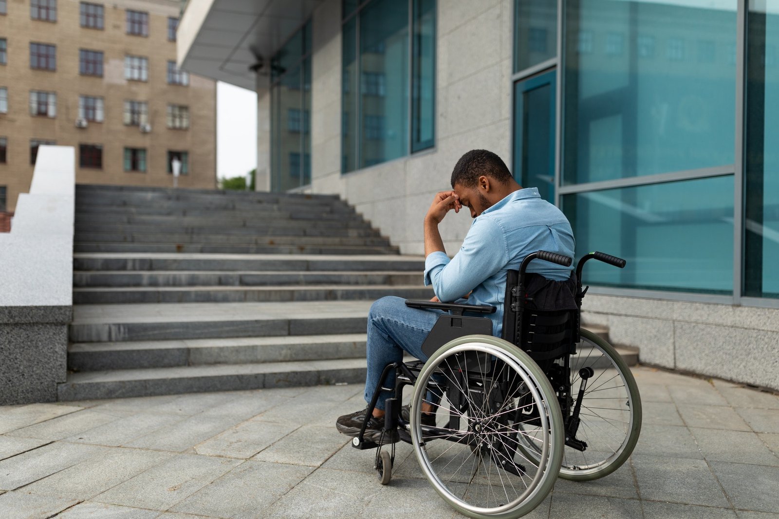 Upset handicapped black man in wheelchair in front of stairs without ramp, having no possibility to